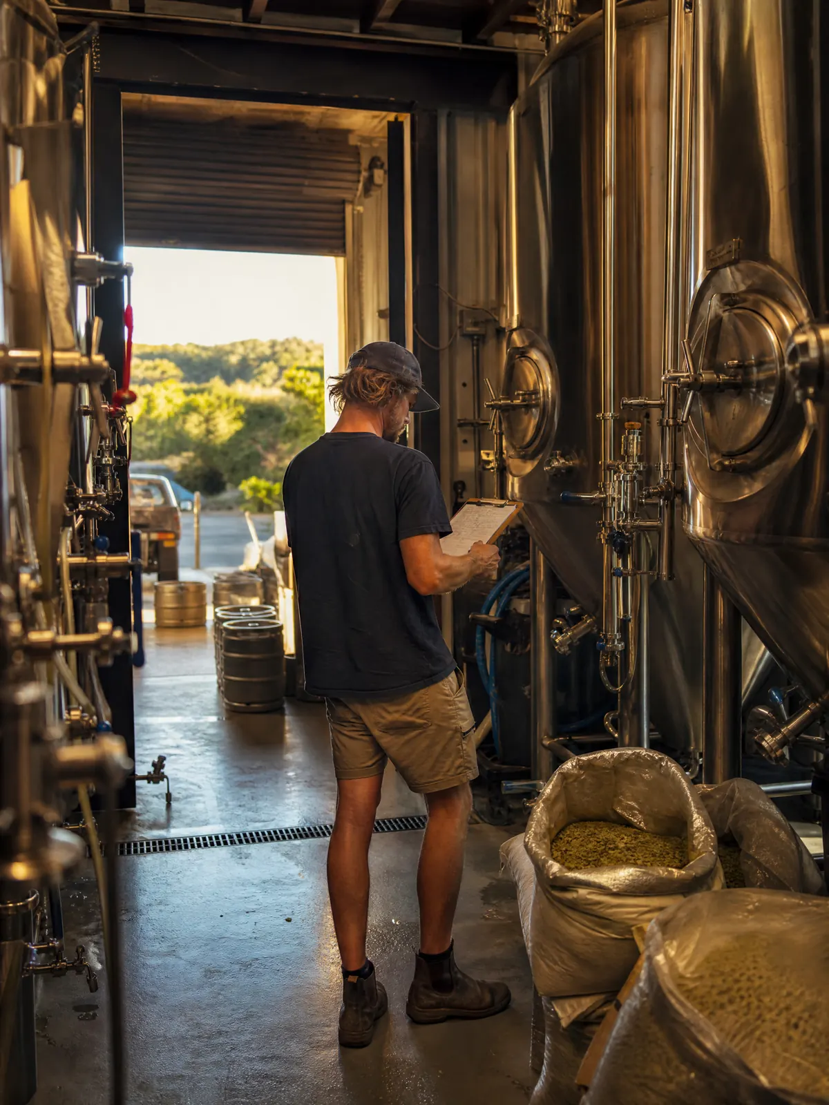 Craft brewery owner checking a clipboard among fermentation tanks