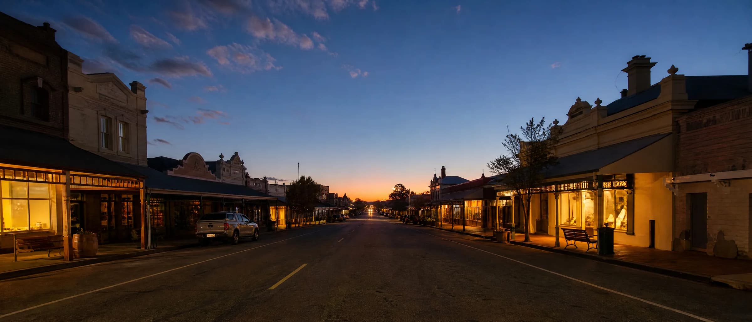 An Australian country-town main street at dusk with small businesses lit up